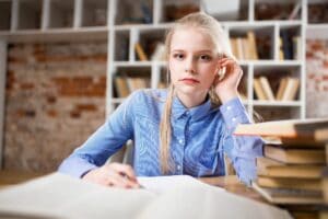 Female in blue shirt next to stack of books.